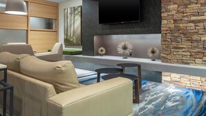 Ein modernes Wohnzimmer mit Steinakzentwand, einem Flachbildfernseher und einem großen Fenster mit Blick auf einen Wald.
