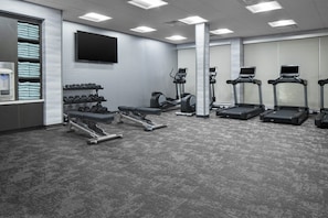 Une salle de sport équipée de tapis de course, de vélos elliptiques, d’haltères et d’un écran de télévision.