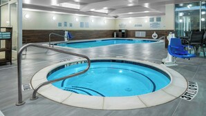Ein großes Hallenbad mit Whirlpool, umgeben von Fliesenboden und ausgestattet mit Sicherheitsgeländern.