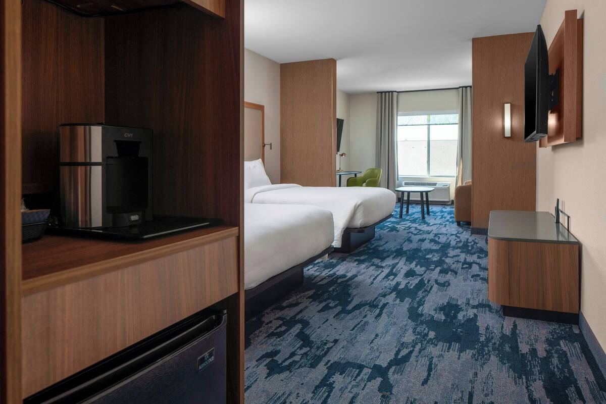 A hotel room with a minibar, a bed, a desk, and a television.