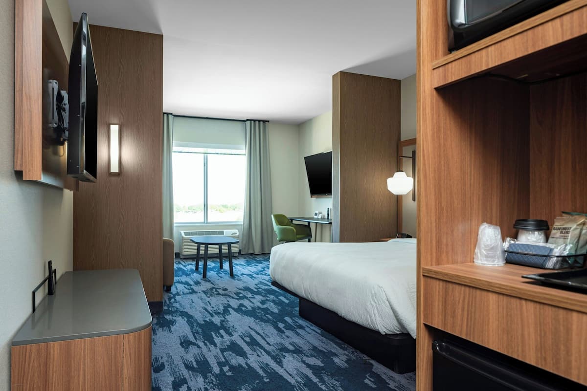 A hotel room with a bed, a desk, a chair, a television, and a window with curtains.