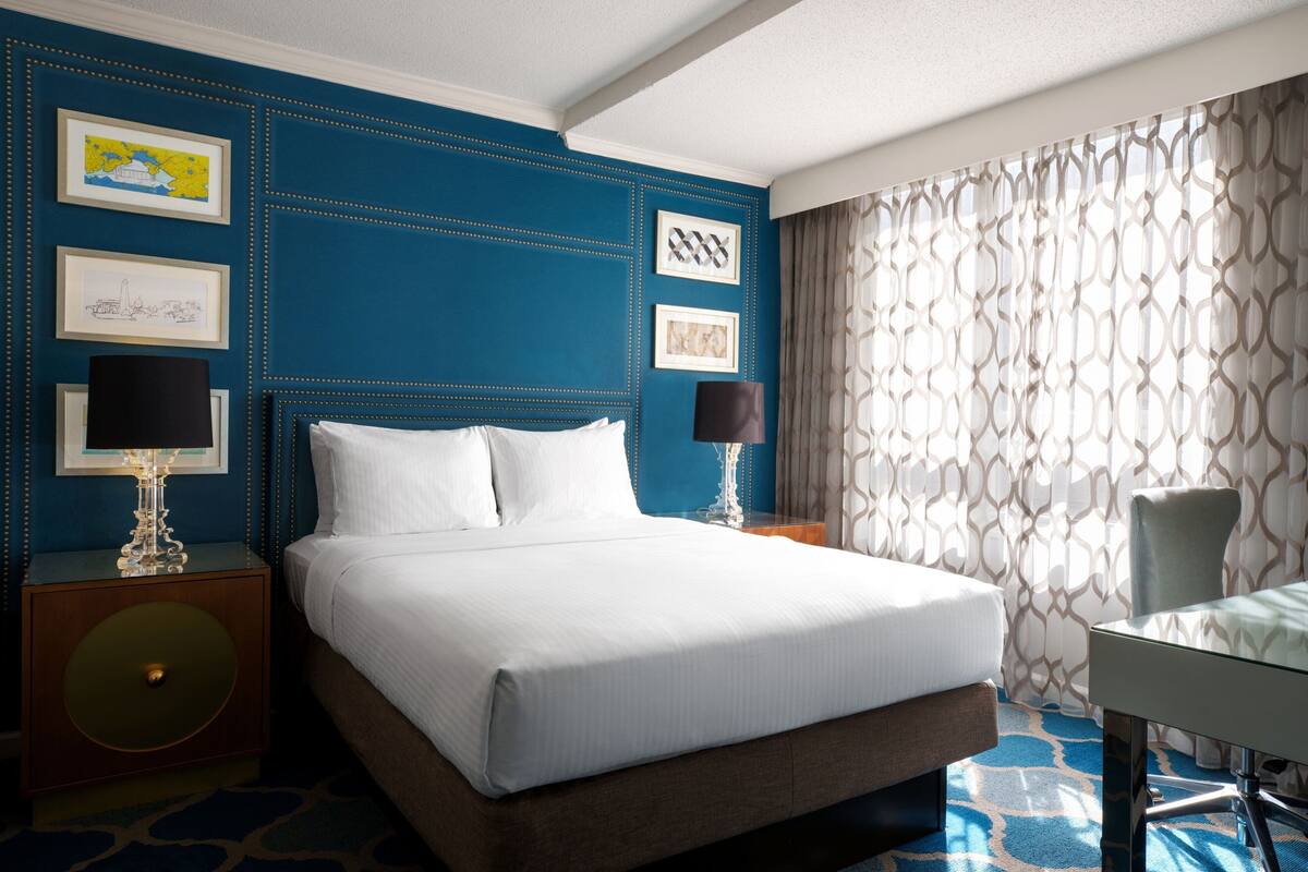 A hotel room with a large bed, two bedside tables with lamps, a desk, and a patterned curtain.