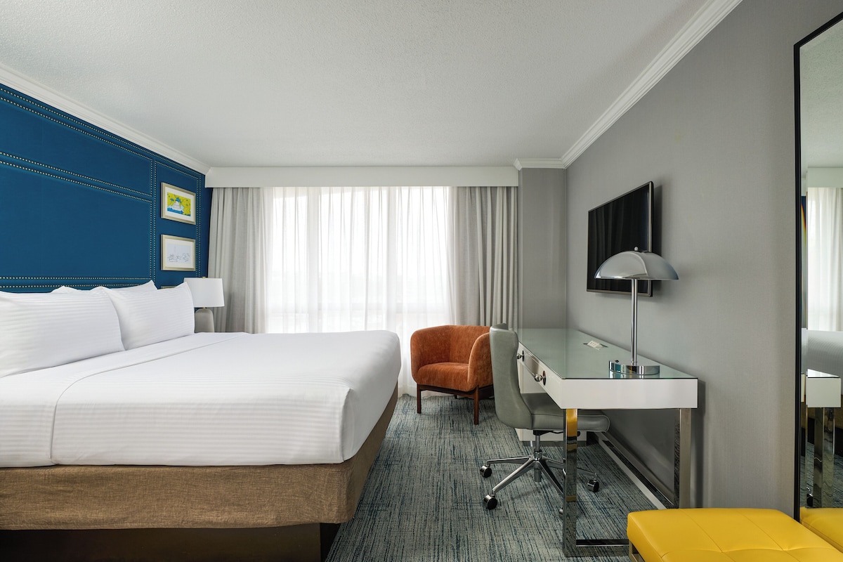 A hotel room with a bed, a desk, a chair, a TV, and a mirror.