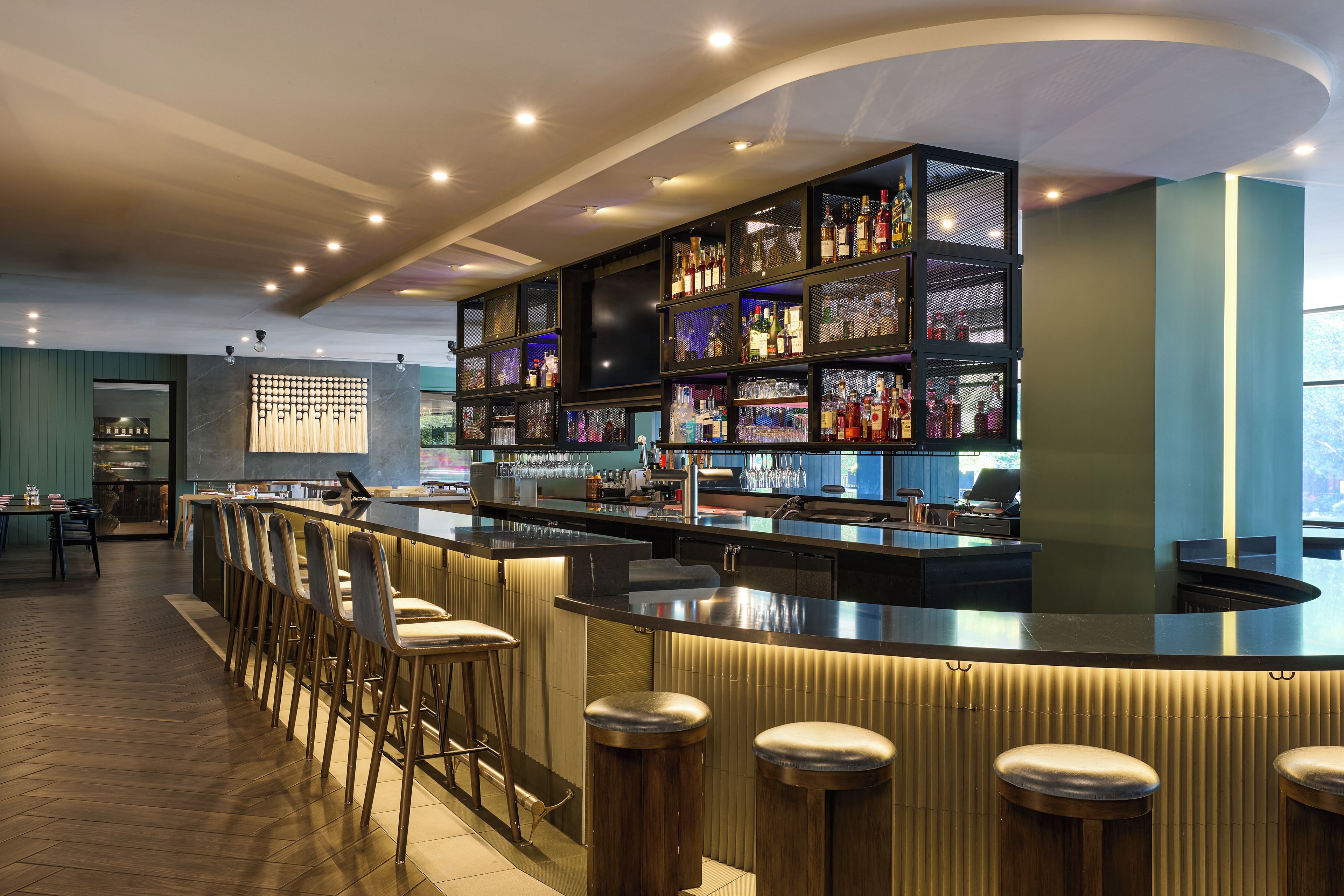 Zona de bar con una barra larga, taburetes y una variedad de botellas y vasos.