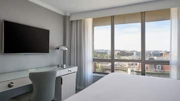 Een hotelkamer met een bed, een bureau, een stoel, een televisie en een groot raam met uitzicht op de stad.