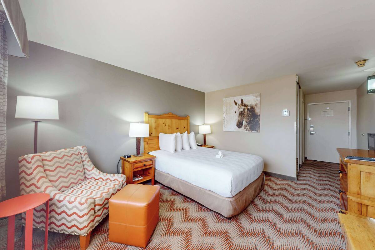 A hotel room with a bed, a chair, a desk, and a lamp.