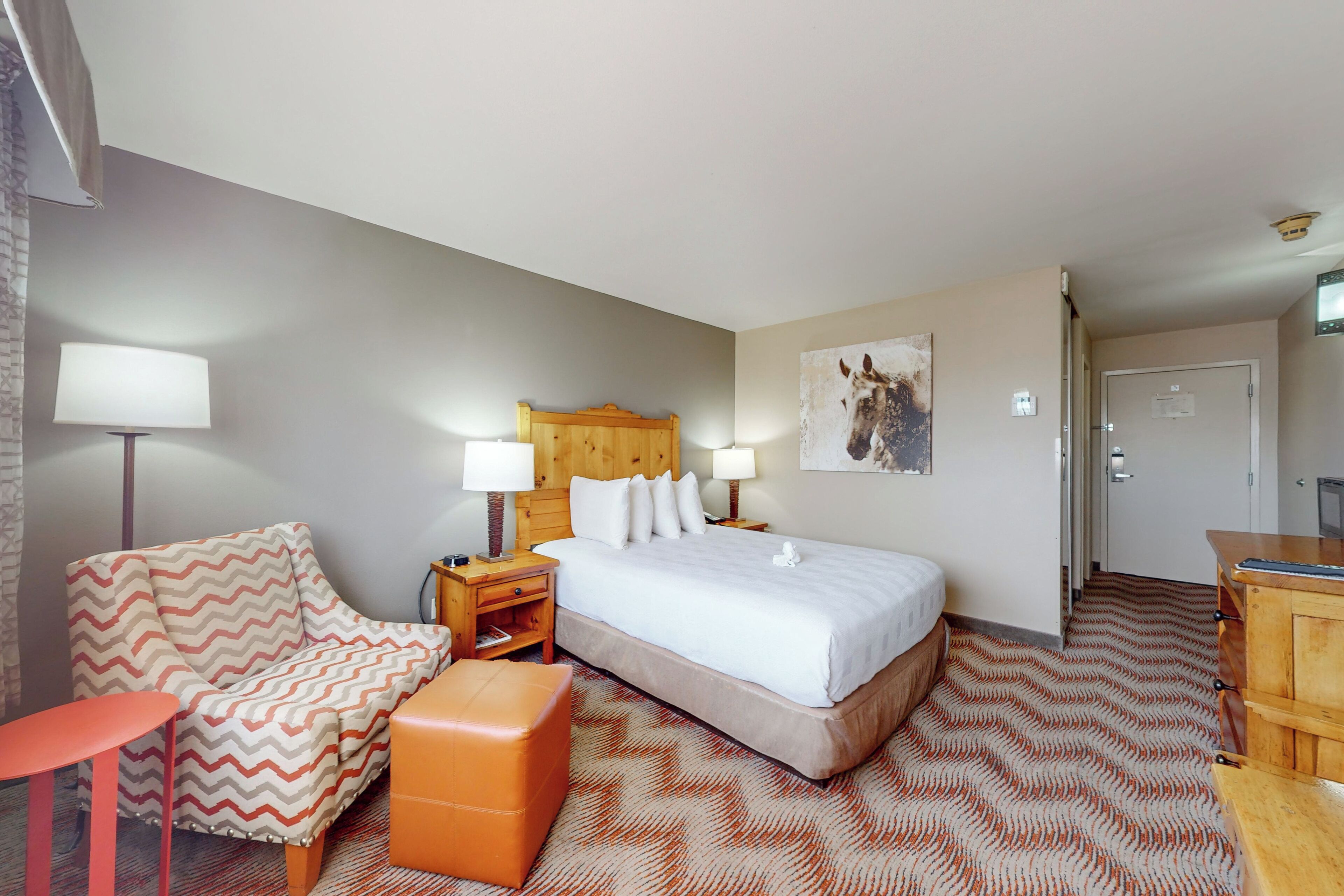 A hotel room with a bed, a chair, a desk, and a lamp.