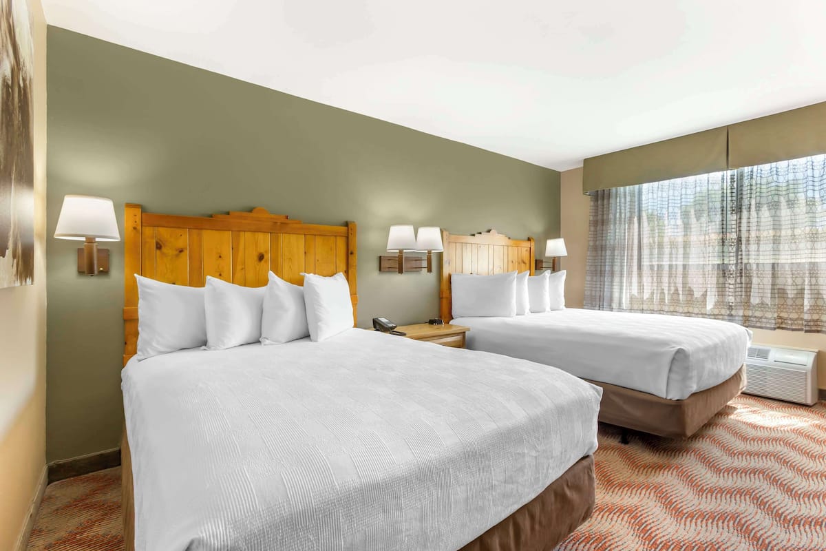 A hotel room with two beds, a wooden headboard, bedside lamps, a telephone, and a window with curtains.