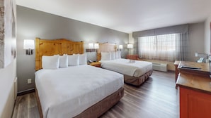 A hotel room with two beds, wooden headboards, bedside lamps, a desk, and a window with curtains.