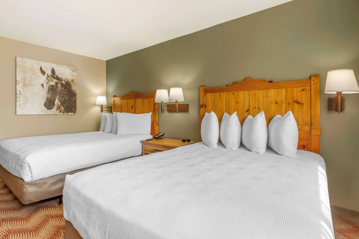 A hotel room with two beds, wooden headboards, white bedding, and a mounted artwork of a horse.
