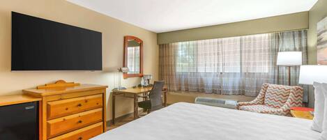 A hotel room with a bed, a desk, a chair, a television, a dresser, and a window with curtains.