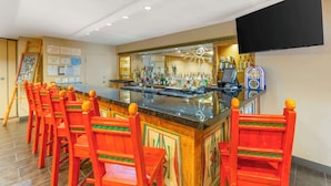 A bar area with a long counter, multiple stools, and a variety of bottles and glasses.