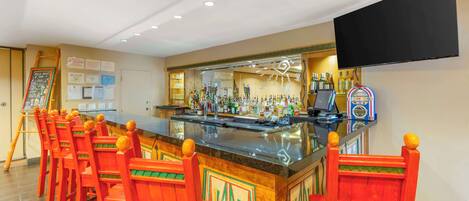 A bar area with a long counter, multiple stools, and a variety of bottles and glasses.