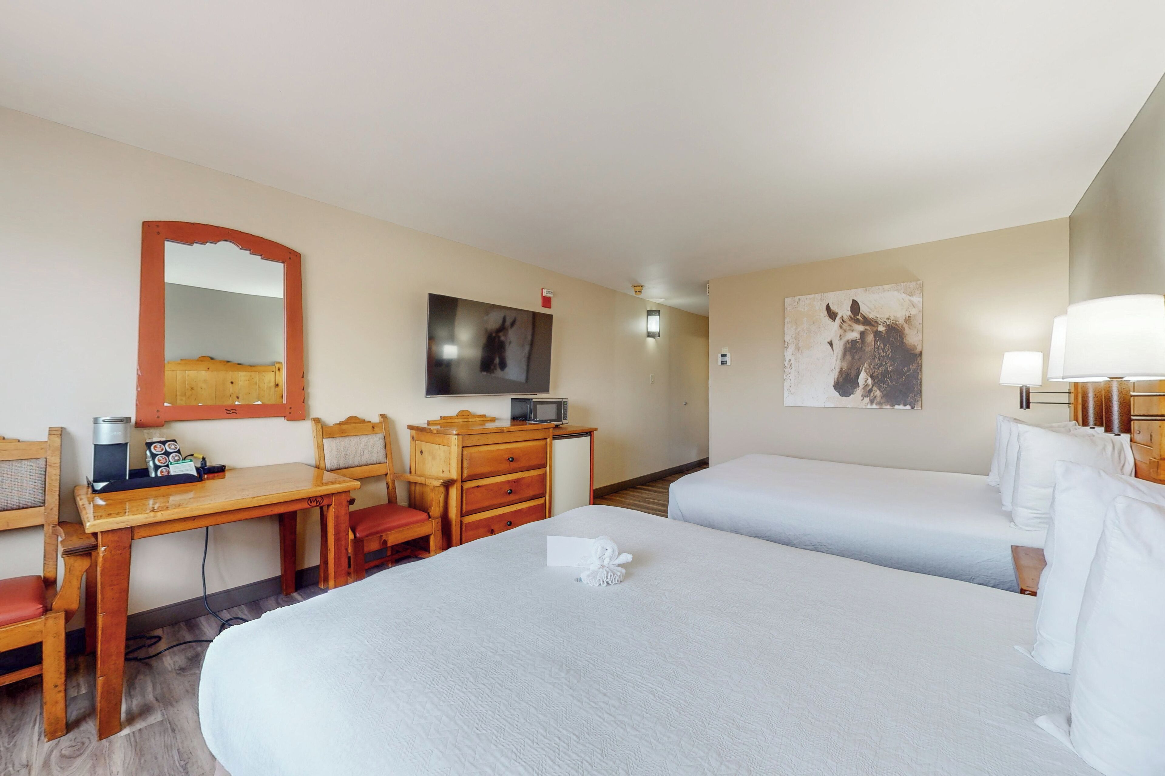 A hotel room with two beds, a desk with a chair, a television, and a painting on the wall.