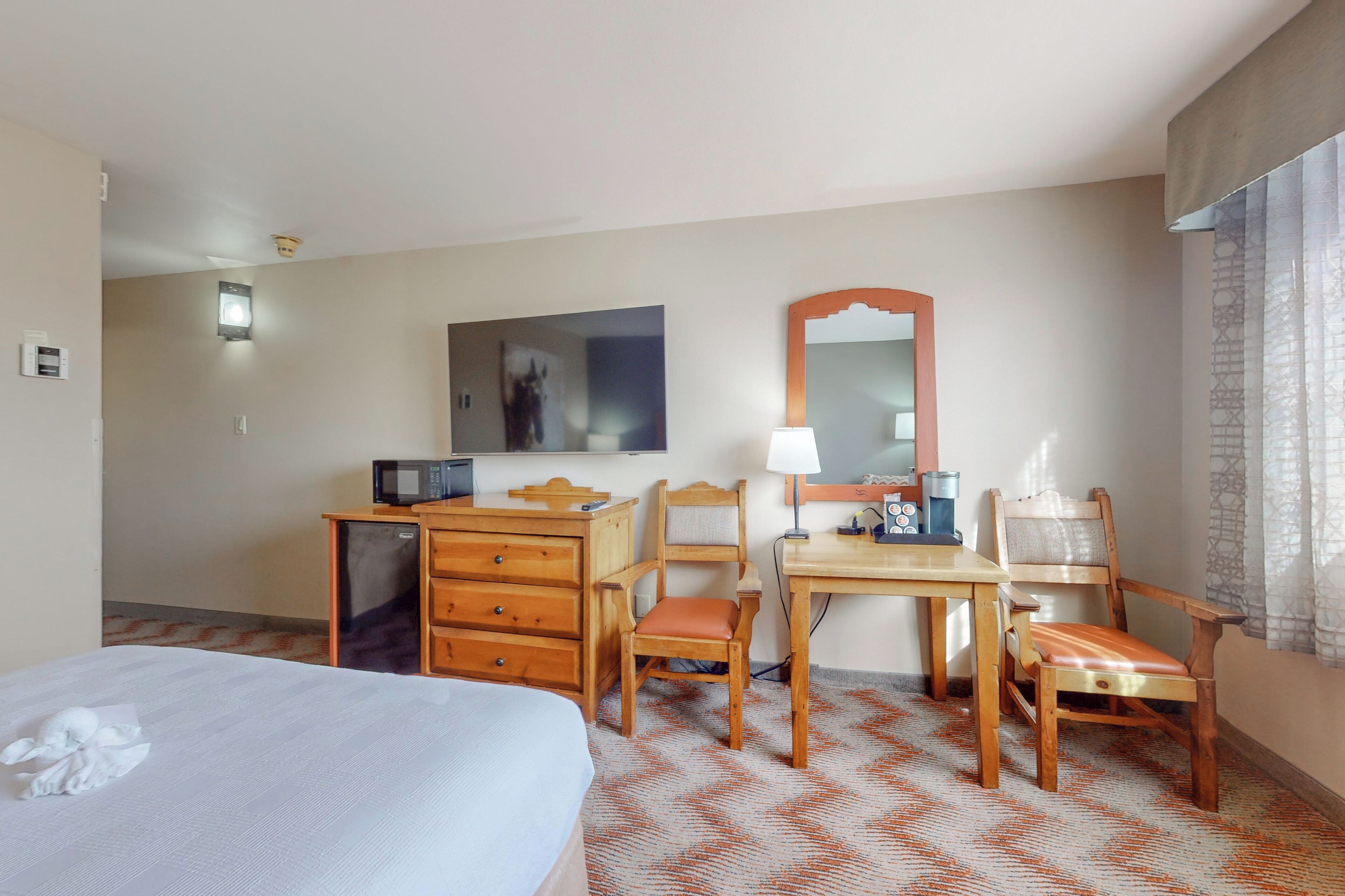 A hotel room with a bed, a desk with a chair, a microwave, a lamp, and a mirror.
