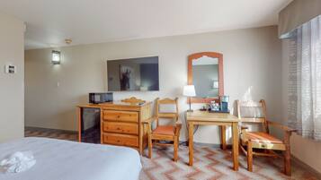 A hotel room with a bed, a desk with a chair, a microwave, a lamp, and a mirror.