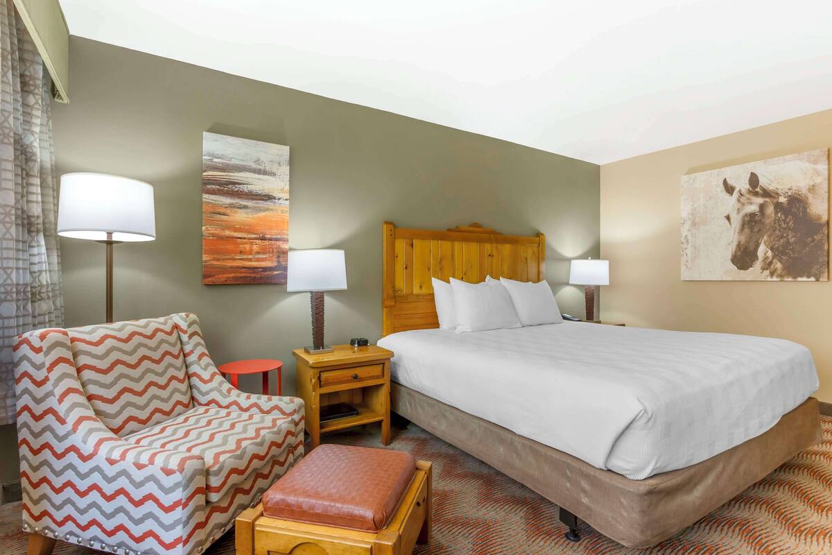 A hotel room with a bed, a chair, a nightstand, and a lamp.