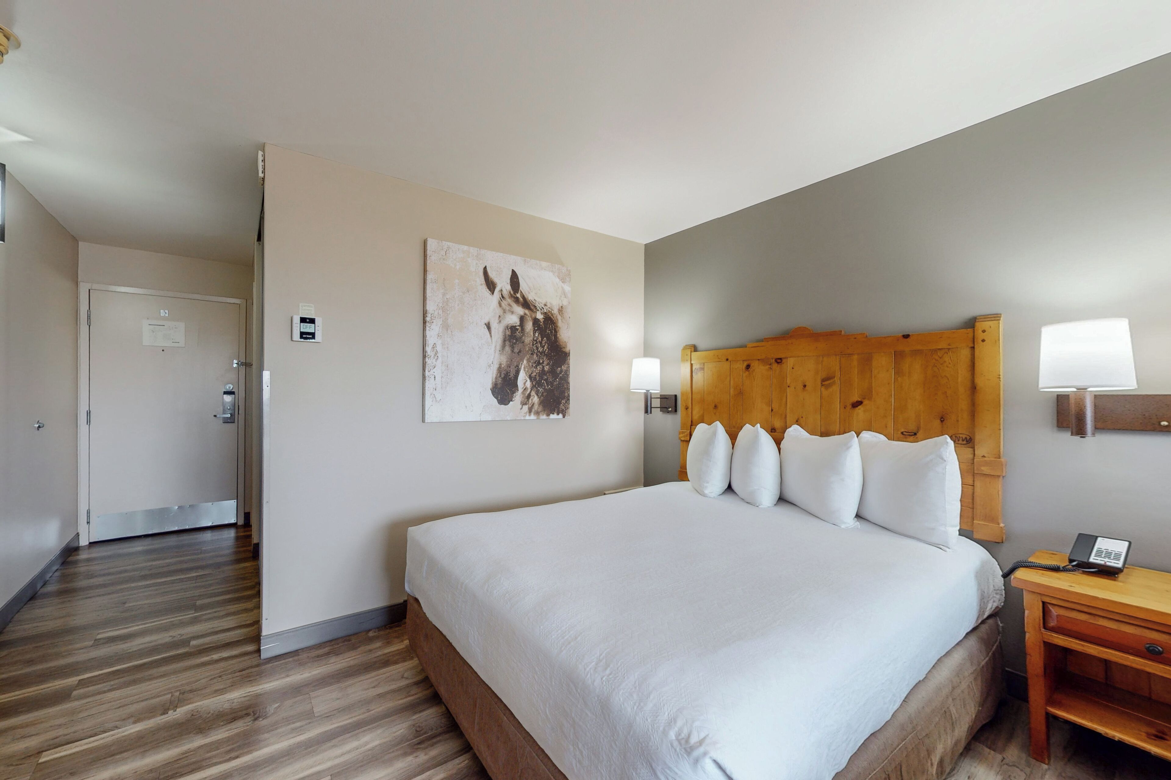 A hotel room with a large bed, wooden headboard, two bedside lamps, a nightstand, and a wall-mounted telephone.