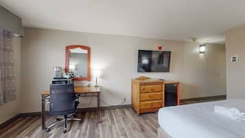 Ein Hotelzimmer mit Schreibtisch aus Holz, einem Sessel, einer Kommode, einem Bett, einem flachbildfernseher an der Wand und einem kleinen Tisch mit Lampe.