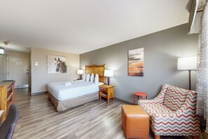 A hotel room with a bed, bedside table, lamp, chair, and artwork on the walls.
