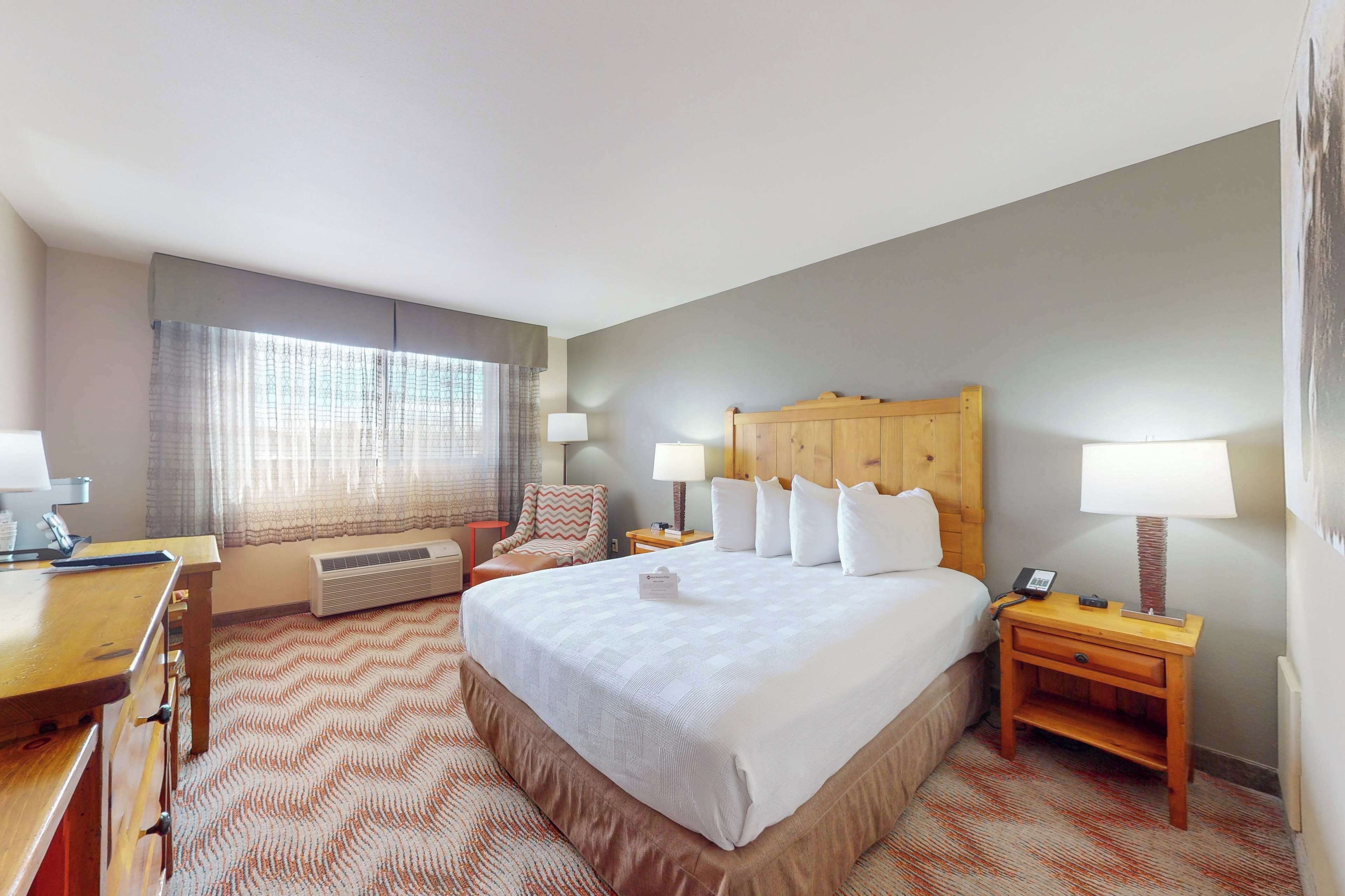 A hotel room with a large bed, a desk, a chair, and a nightstand with lamps.