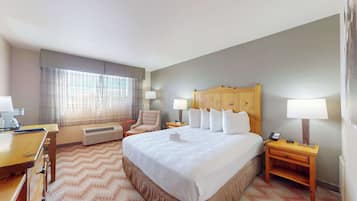 A hotel room with a large bed, a desk, a chair, and a nightstand with lamps.