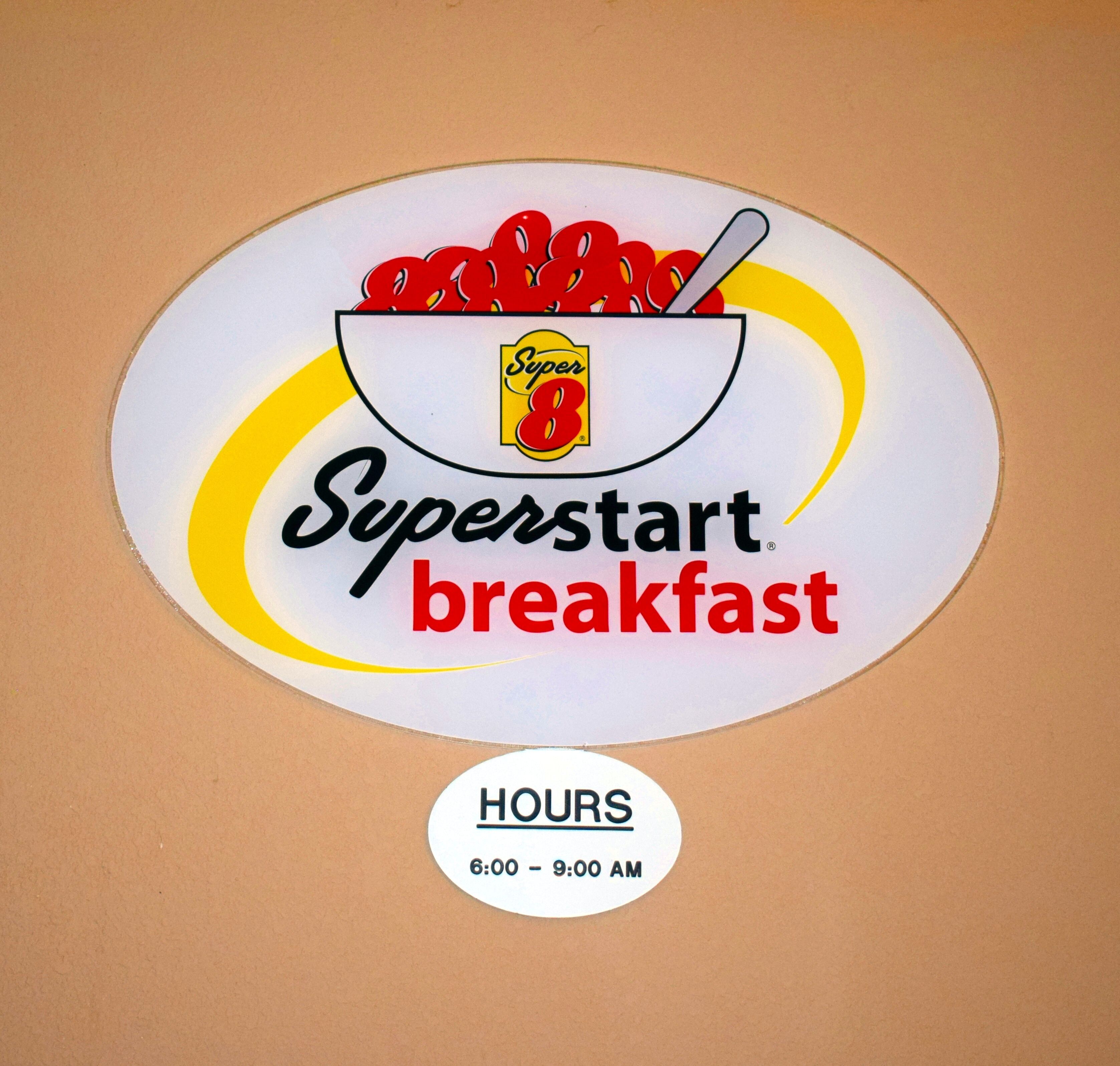 Placa do café da manhã Superstart, com um prato de comida e uma colher, e horário de funcionamento das 6h às 9h.