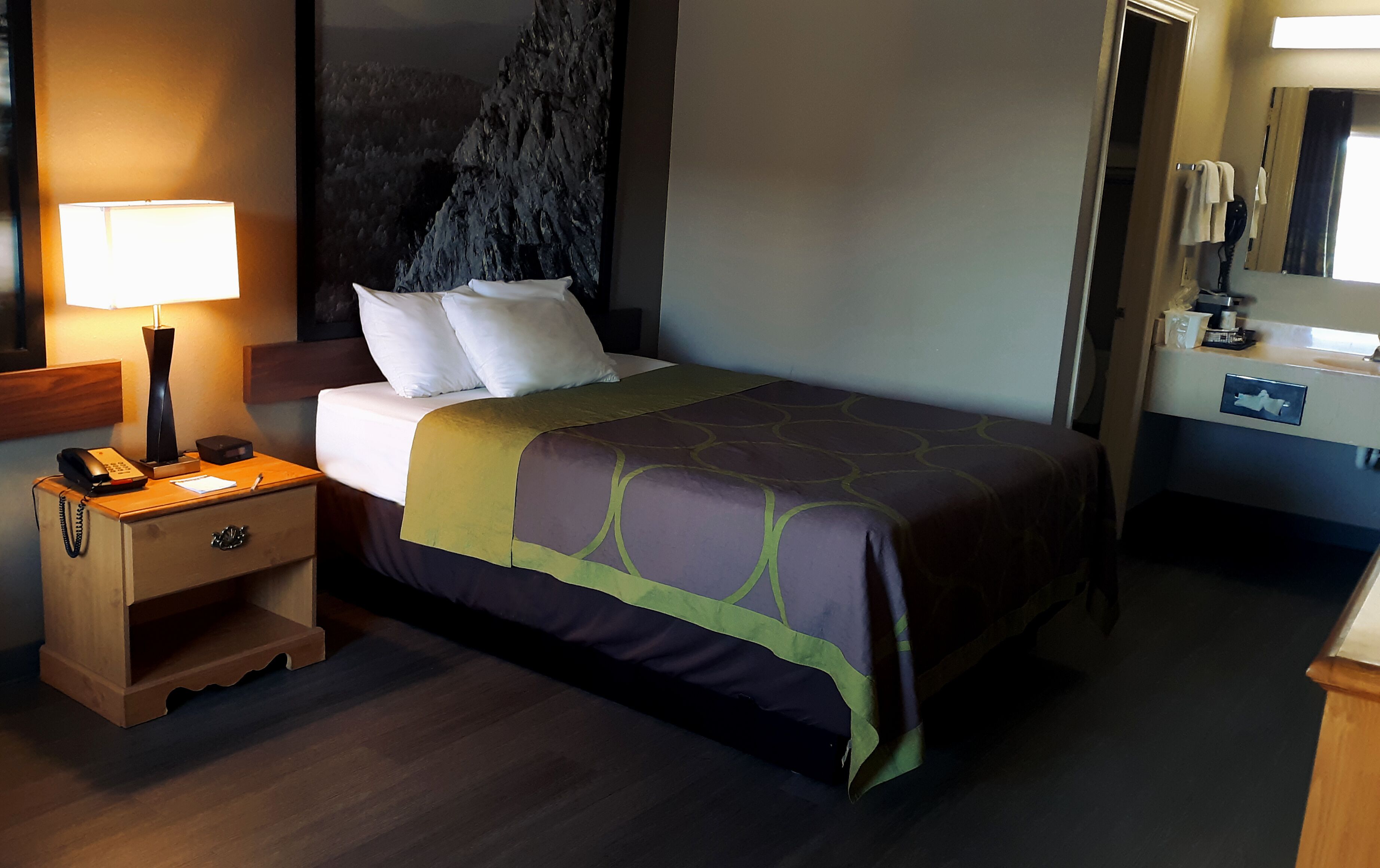 A hotel room with a bed, bedside table, lamp, and a large mirror.