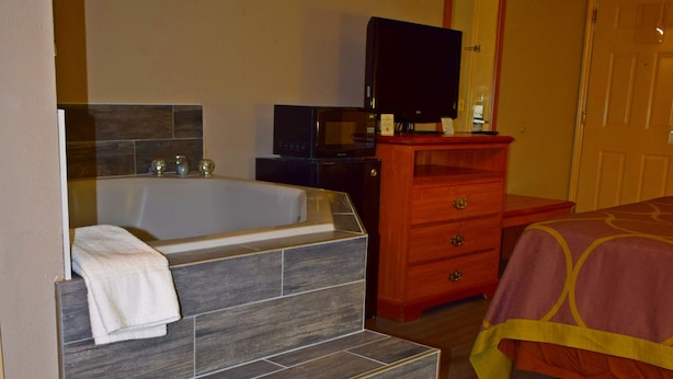 Un baño con una bañera, un tocador de madera, un televisor y una cama con colcha roja y amarilla.
