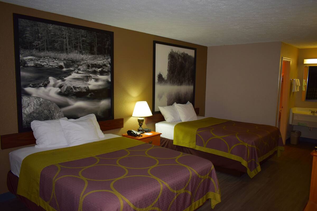 Habitación de hotel con dos camas, una mesita de noche con lámpara y dos cuadros grandes en la pared.