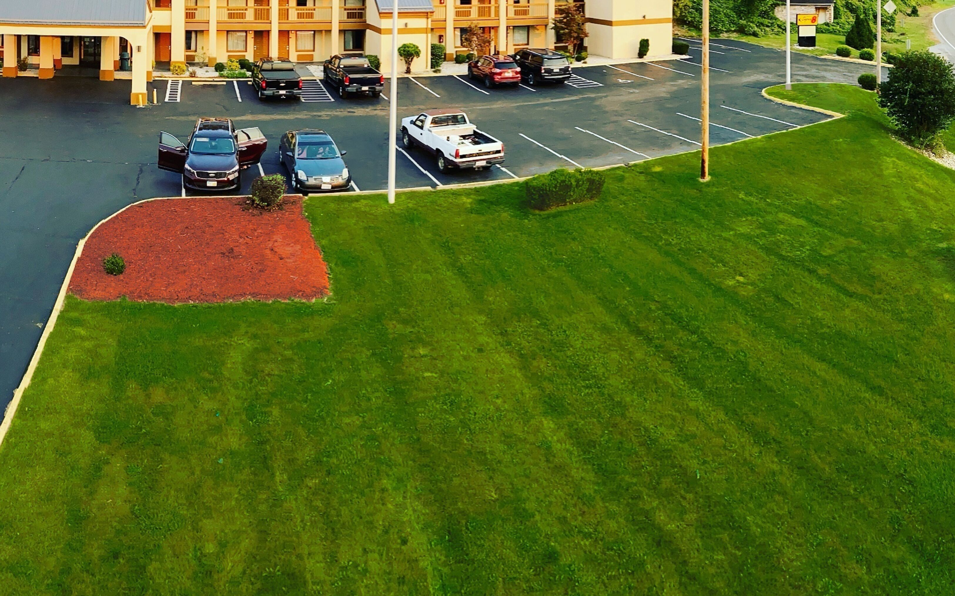 An aerial view of a parking lot with several cars, a building with a yellow facade, and a well-maintained grassy area.
