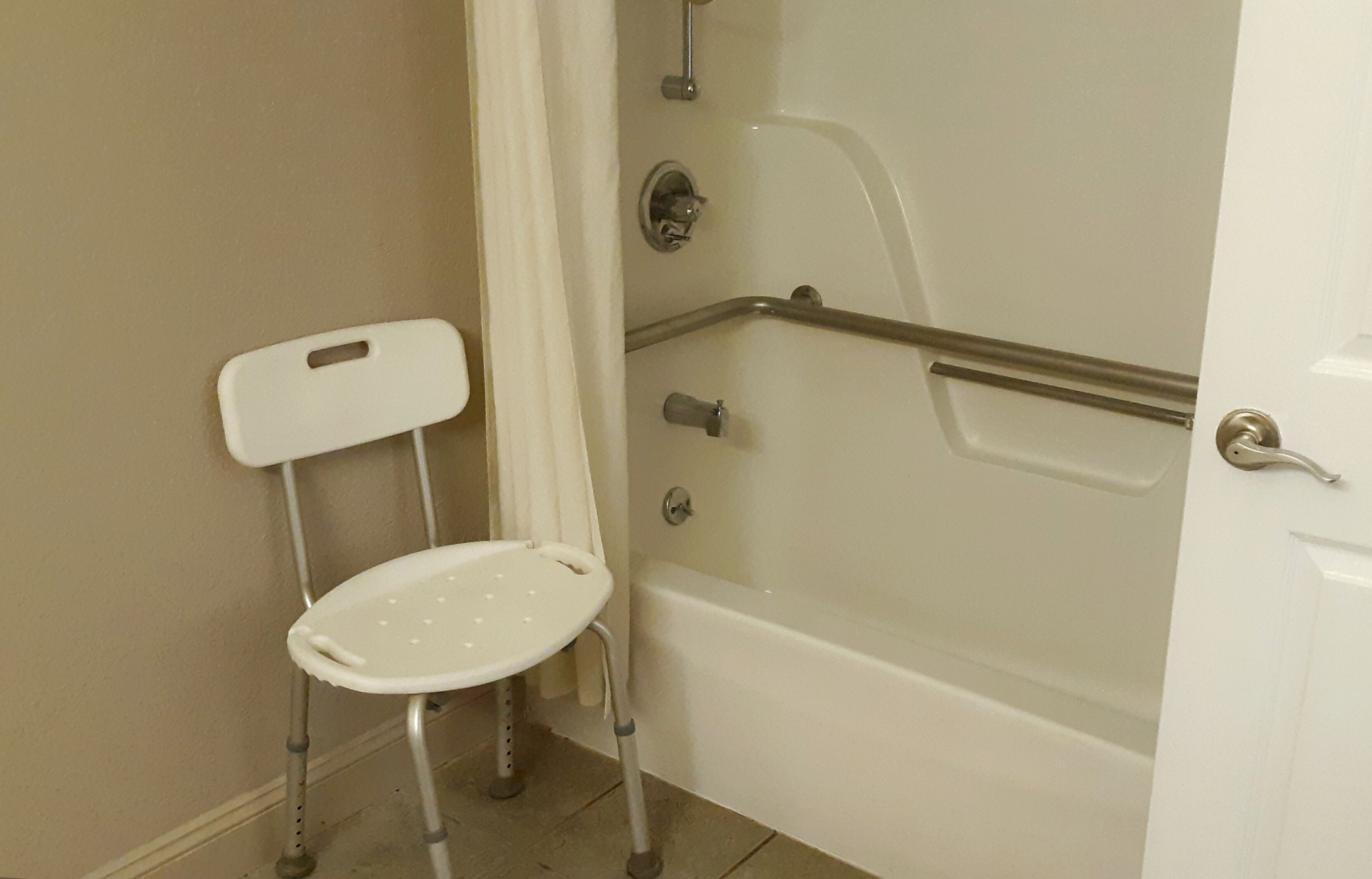 A bathroom with a white bathtub, a white toilet, and a white chair with armrests.