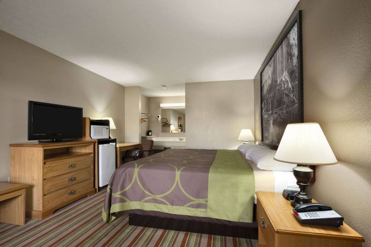 Habitación de hotel con cama, televisor, escritorio con computadora, lámpara y teléfono.