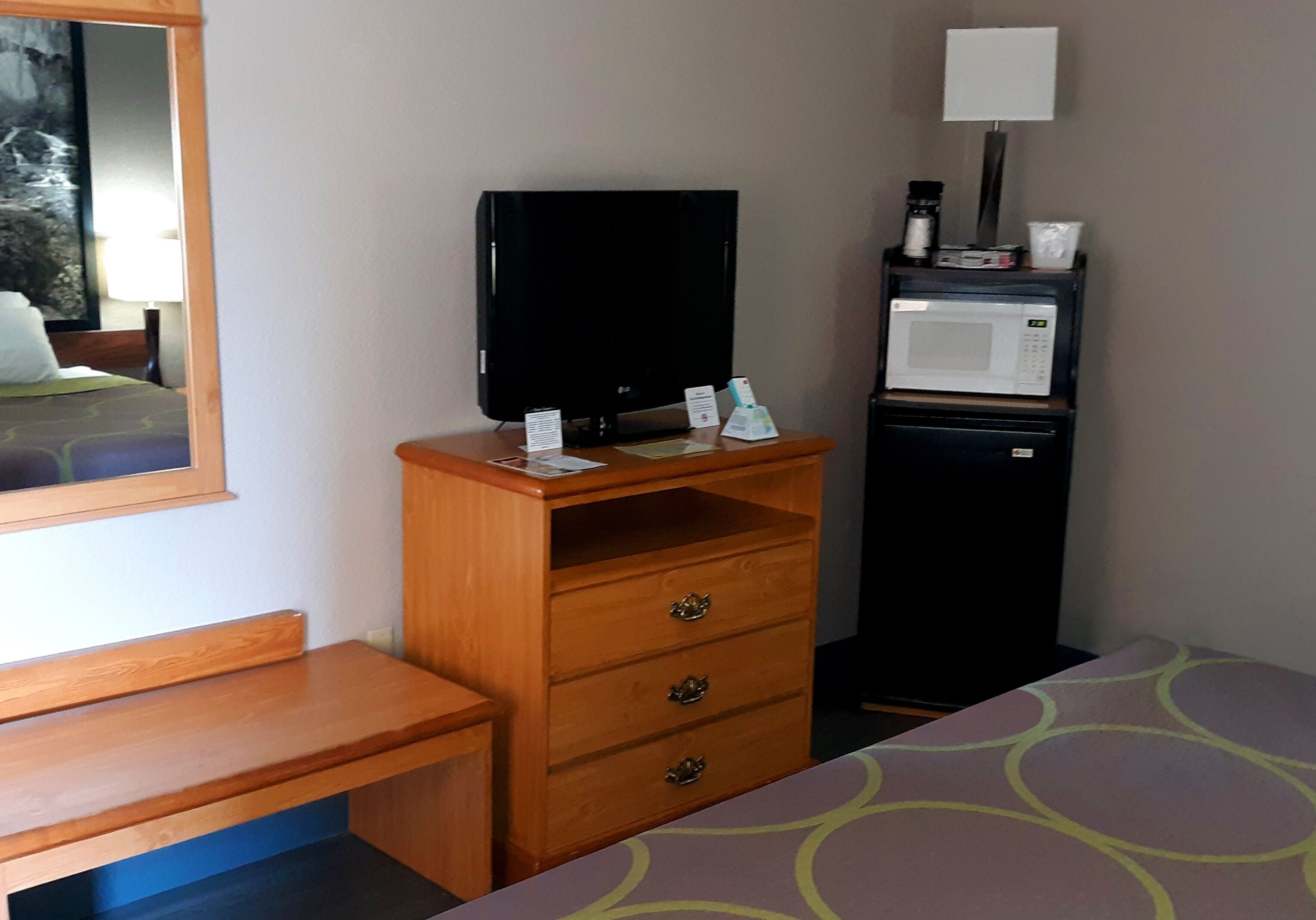 Una habitación de hotel con un escritorio de madera, un televisor, un microondas y una cama con una colcha estampada.