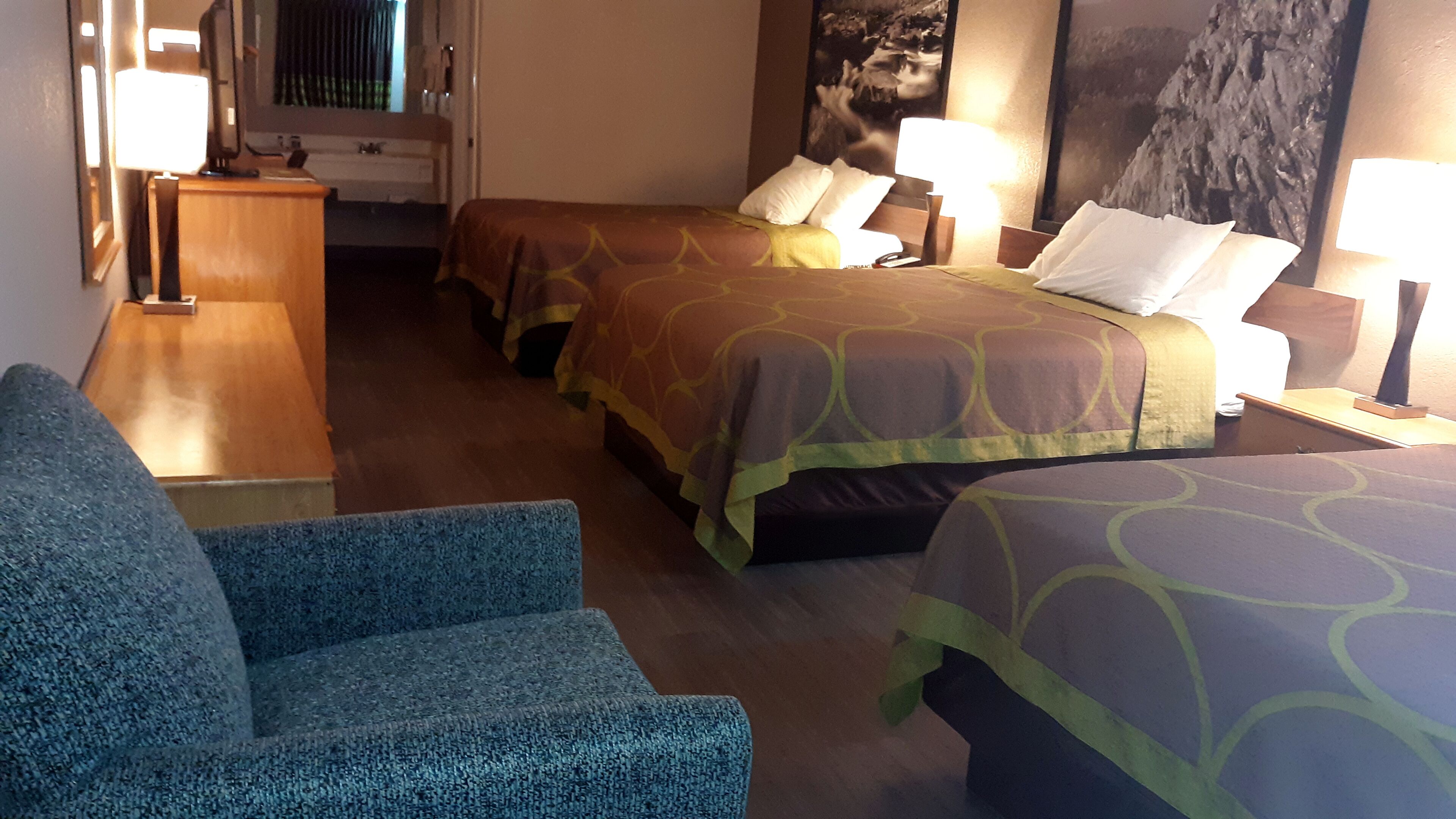 Quarto de hotel com duas camas, uma escrivaninha, uma cadeira e um quadro grande na parede.