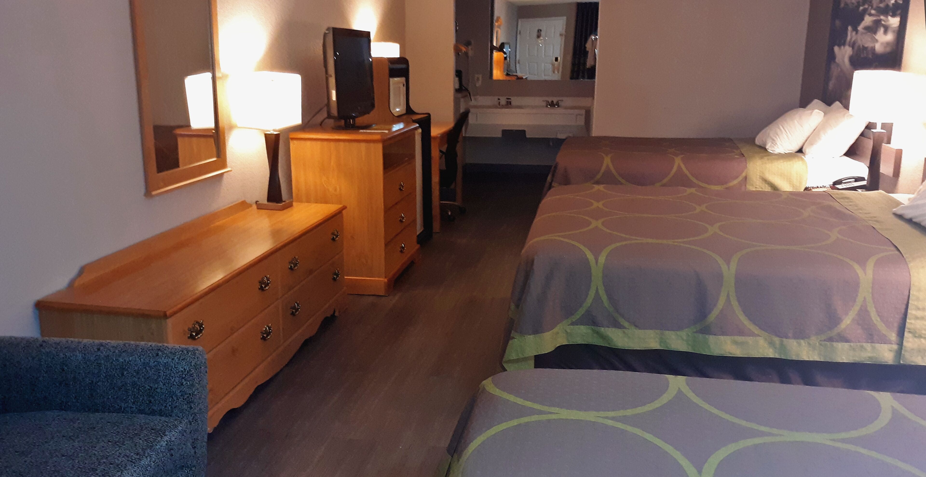 A hotel room with a bed, a dresser, a mirror, and a desk.