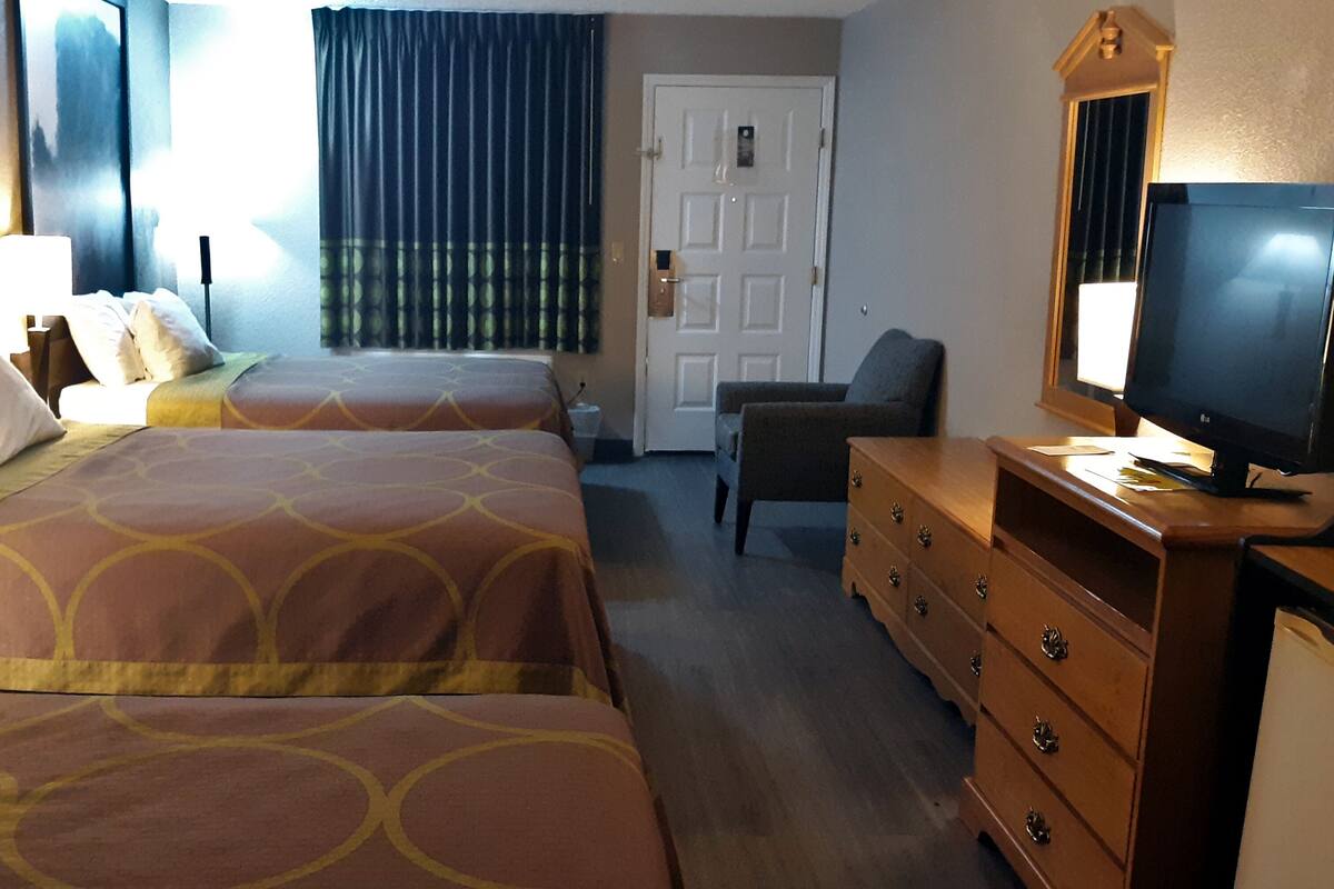 Habitación de hotel con dos camas, un aparador, un televisor y una puerta.