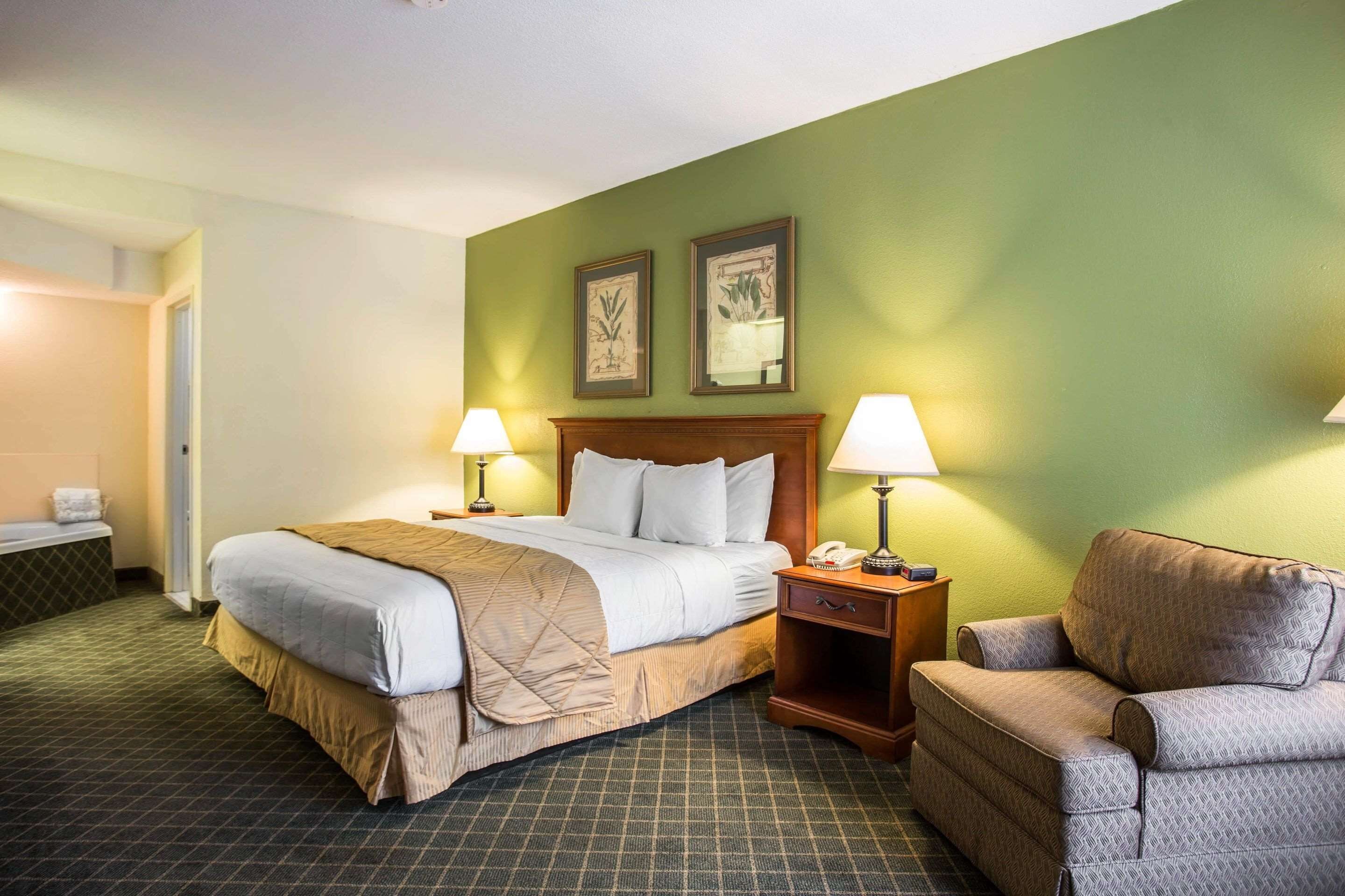 A hotel room with a bed, two bedside lamps, a nightstand, a chair, and two framed pictures on the wall.