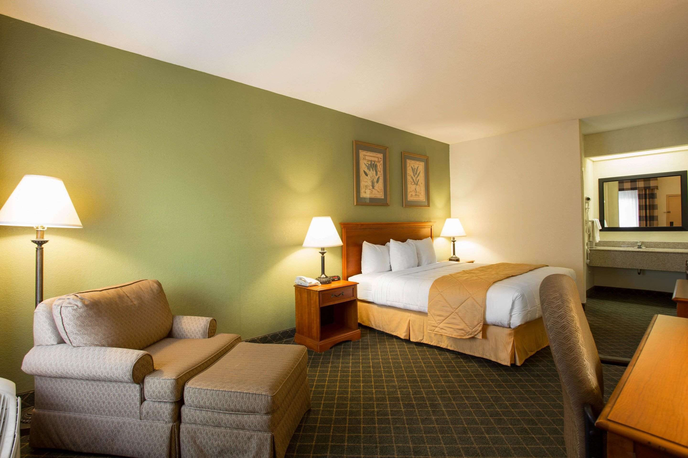 Una habitación de hotel con una cama, dos mesitas de noche con lámparas, una silla y un escritorio.