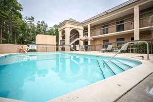 A swimming pool with a lifeguard station, a covered seating area, and a multi-story building with balconies.