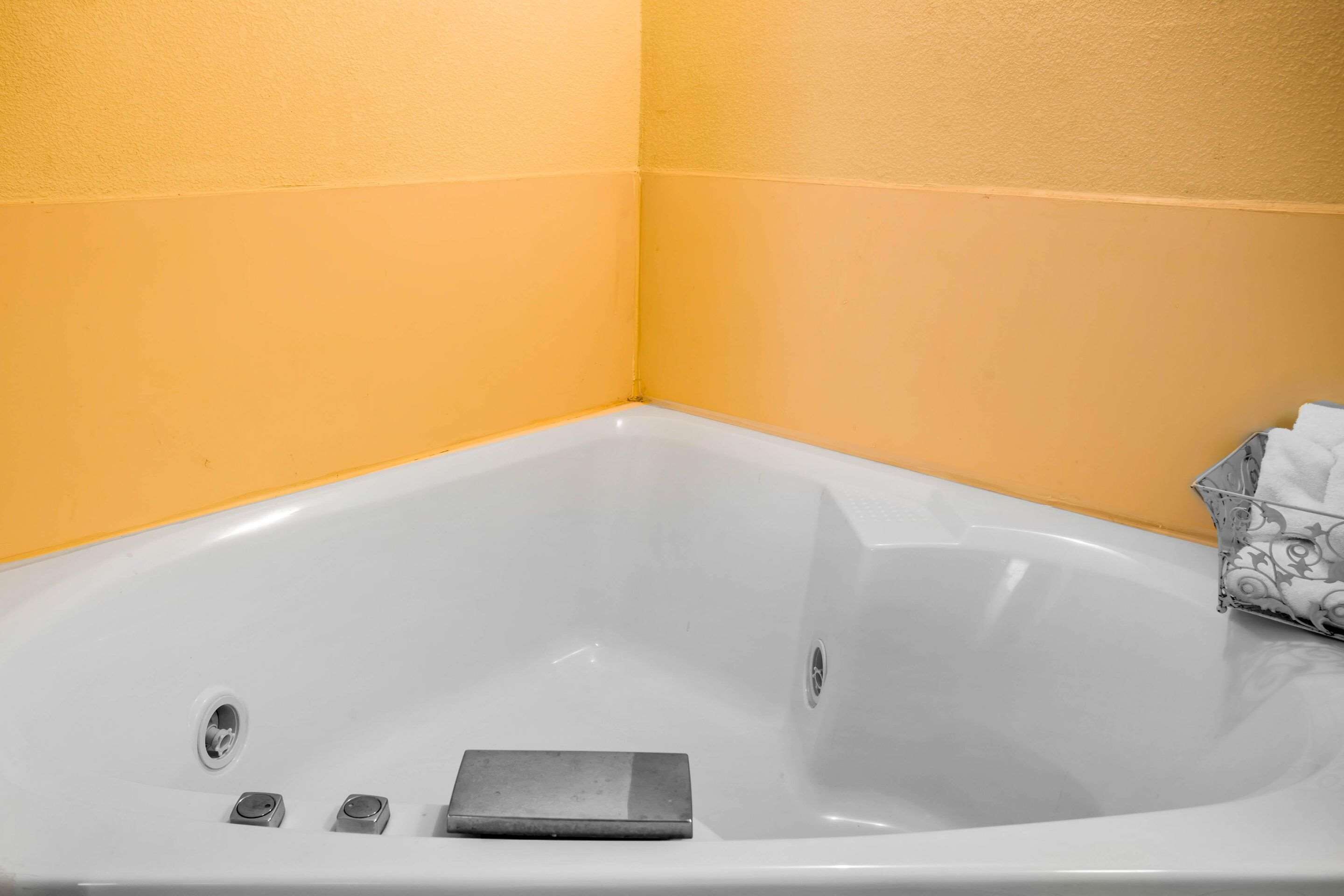 A corner bathtub with a drain, a control panel, and a towel rack with a towel.