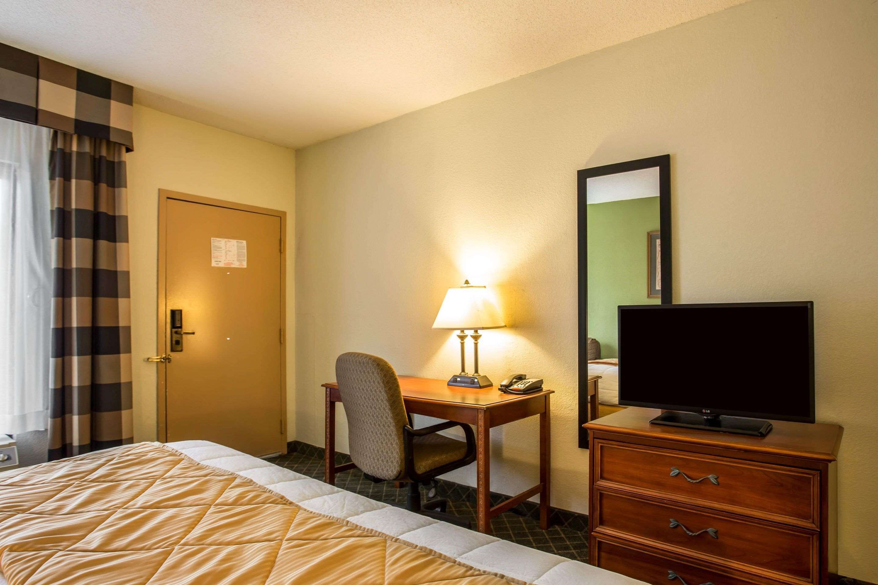 Una habitación de hotel con cama, escritorio con lámpara, televisor en una cómoda y puerta con un cartel.