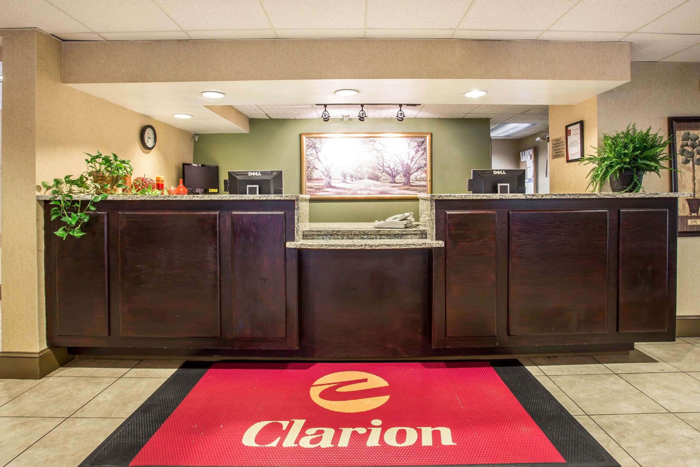 A reception area with a dark wood reception desk, a red carpet with the Clarion logo, a clock on the wall, and a framed picture above the desk.