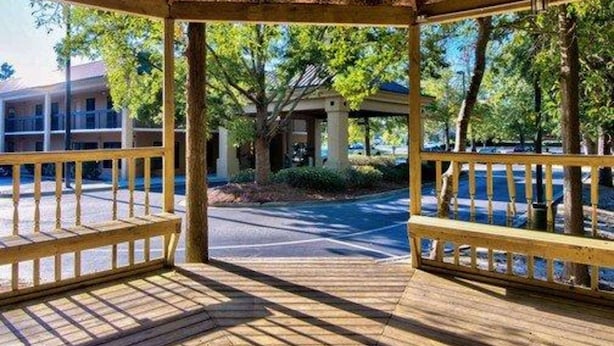 Un kiosque en bois avec un toit de chaume, entouré d’arbres et d’un parking.