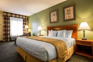 A hotel room with a large bed, two bedside tables with lamps, a chair, and a window with curtains.