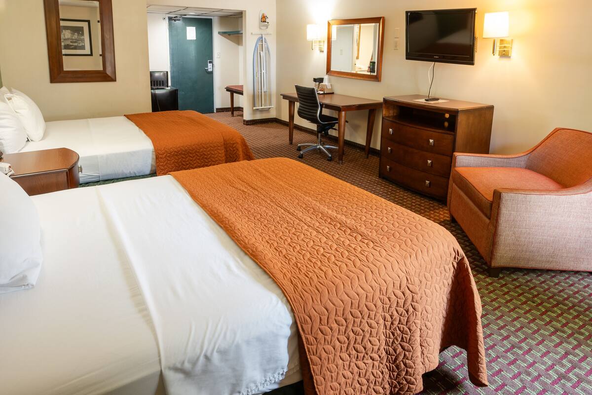 A hotel room with two beds, a desk, a chair, a TV, and a dresser.