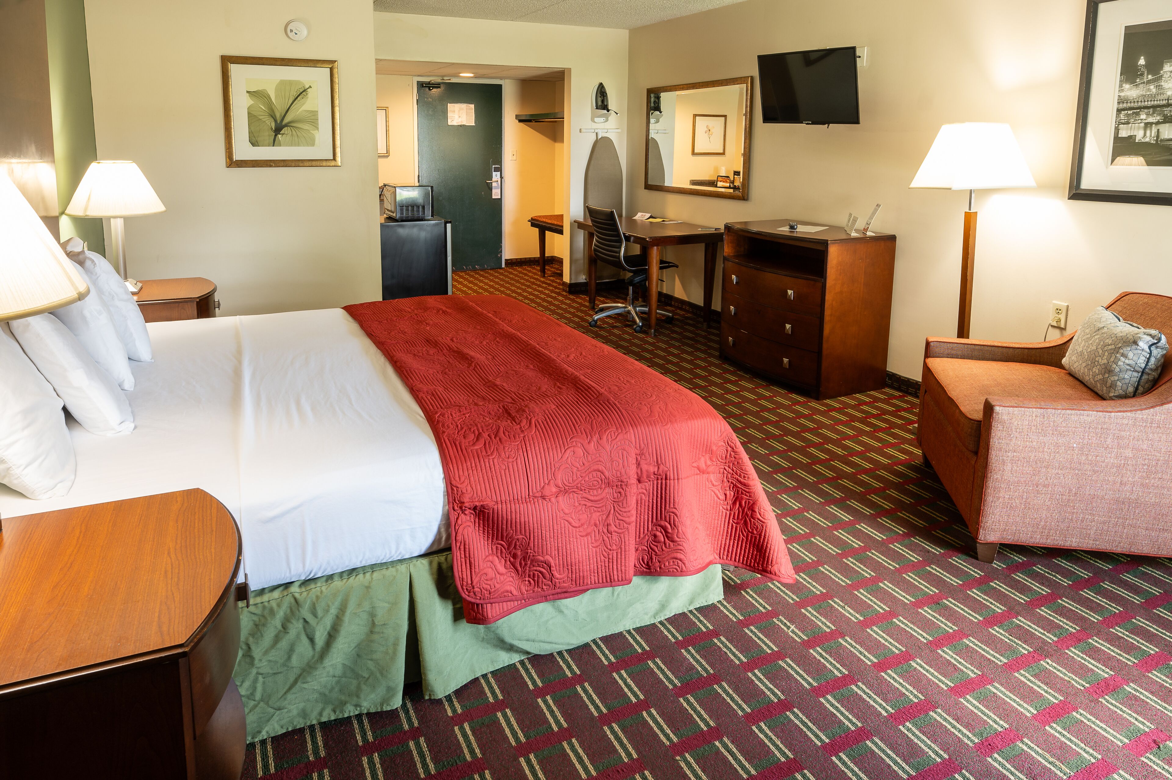 A hotel room with a bed, desk, chair, dresser, and a TV on the wall.
