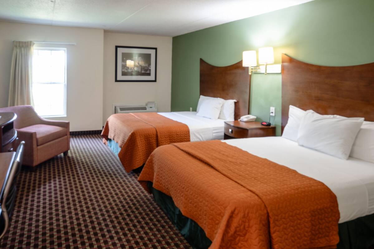 A hotel room with two beds, a desk, a chair, a television, and a window with curtains.