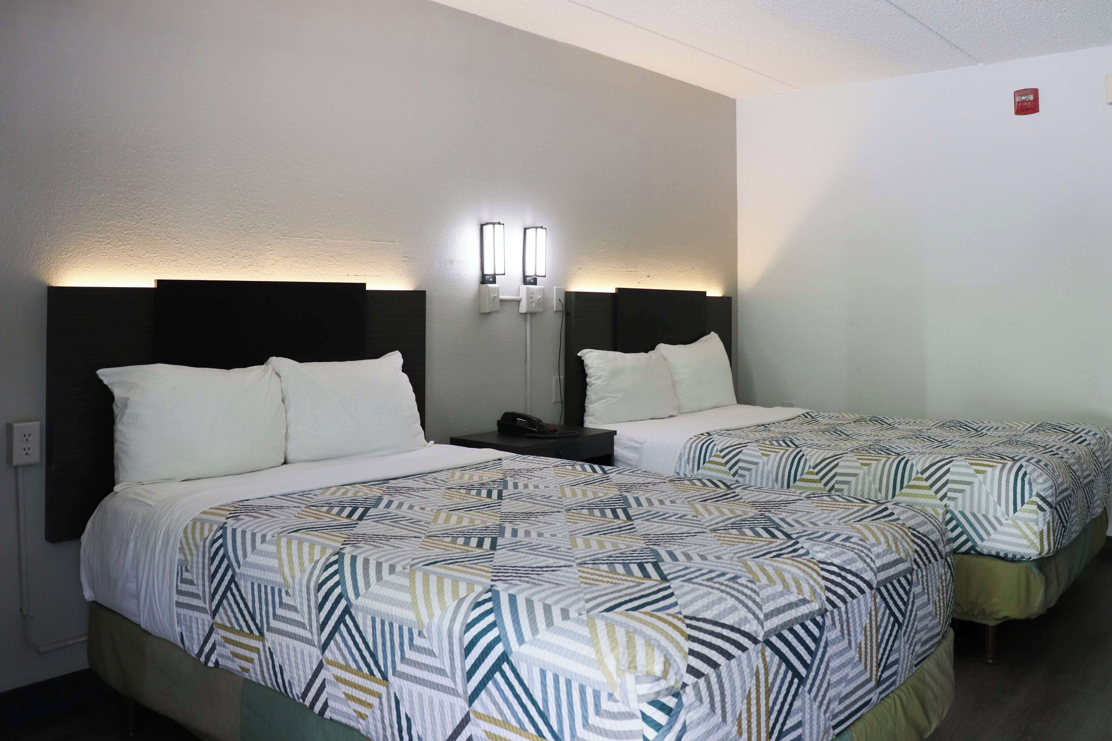 A hotel room with two beds, each with a patterned bedspread, a nightstand, and wall-mounted reading lights.