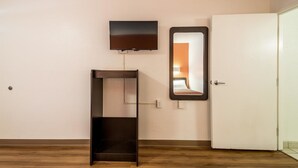 A room with a wooden floor, a white door, a wall-mounted TV, and a mirror reflecting a bed. - Motel 6 Birmingham, AL (Birmingham)